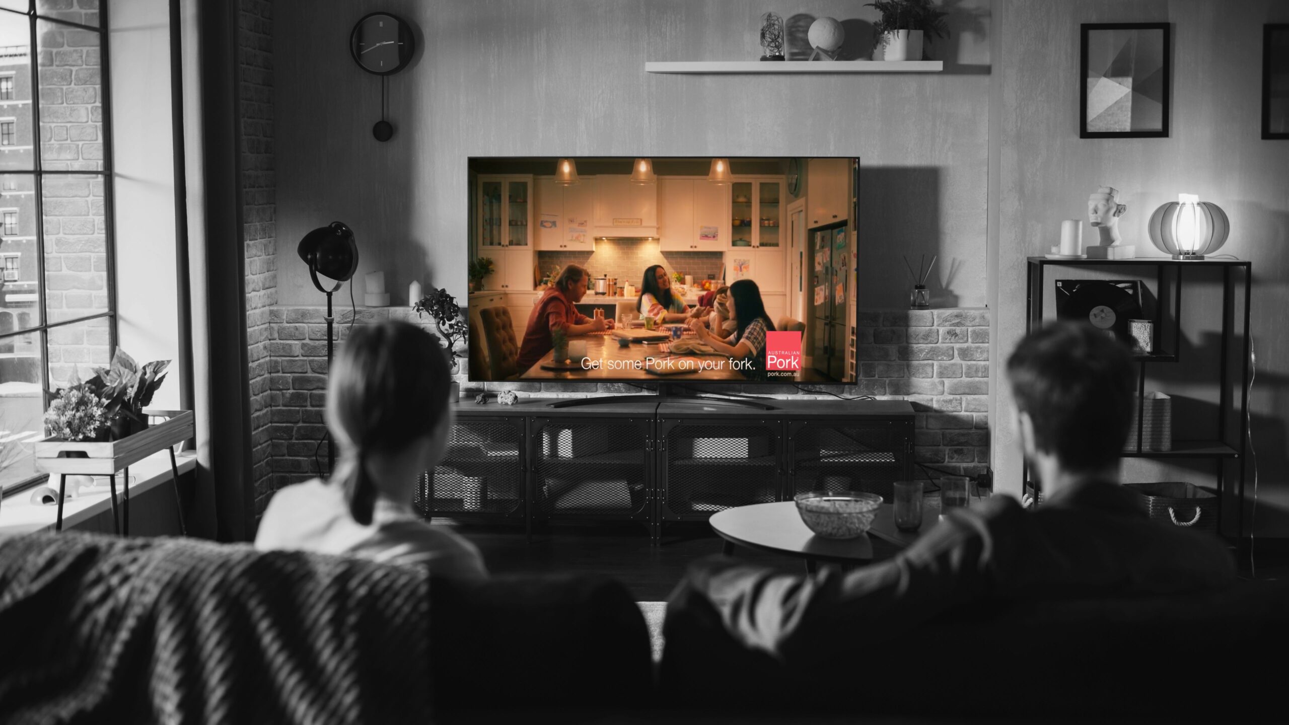 People sitting on a couch watching a pork commercial on TV