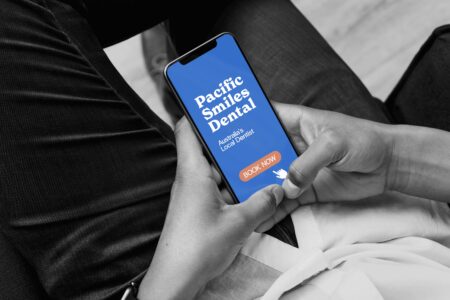A person sitting down and using both hands to hold their phone.