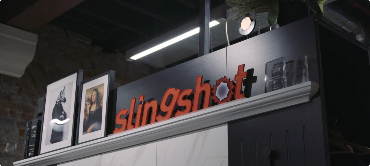 A mantlepiece with framed photos and a sign that says Slingshot.