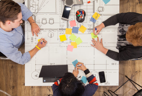 Three people sitting at a table with a blueprint and colourful post-it notes