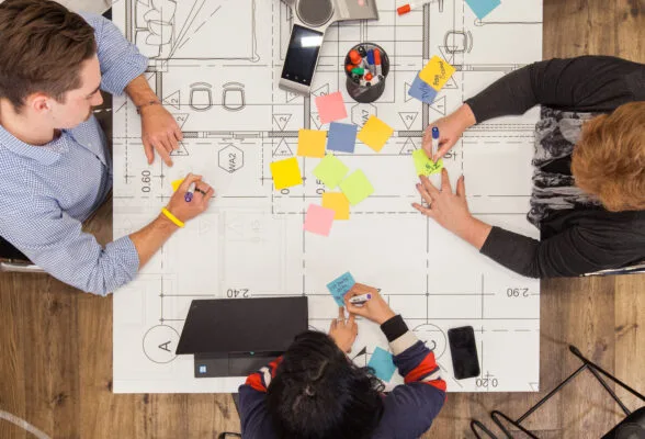 Three people sitting at a table with a blueprint and colourful post-it notes